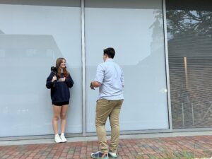 Heather Wright, Fred T Foard High ‘25, stands in front of a building holding a camera as she interviews Andy Bowman, North Buncombe High ‘25 outside the Curtis Media Center.